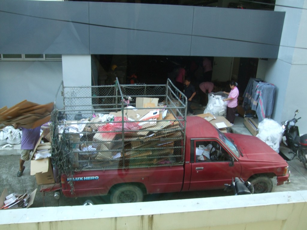 This man bought cardboard to recycle. The ladies weighed it, and then he tossed it onto the back of his truck. 